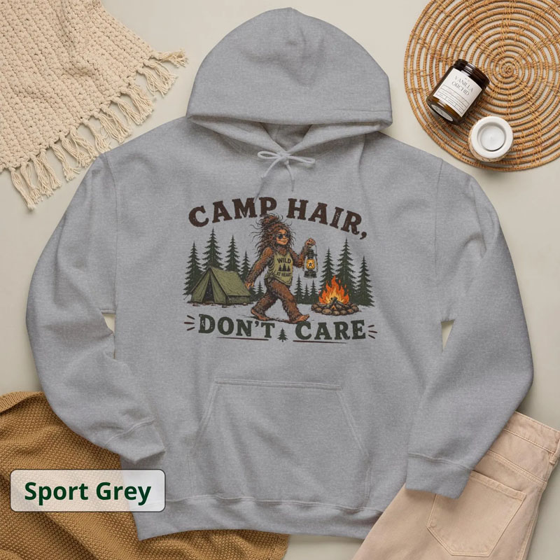 Sport Grey hoodie with a vintage graphic of Bigfoot wearing sunglasses, holding a lantern by a campfire near a tent with text reading CAMP HAIR DON'T CARE