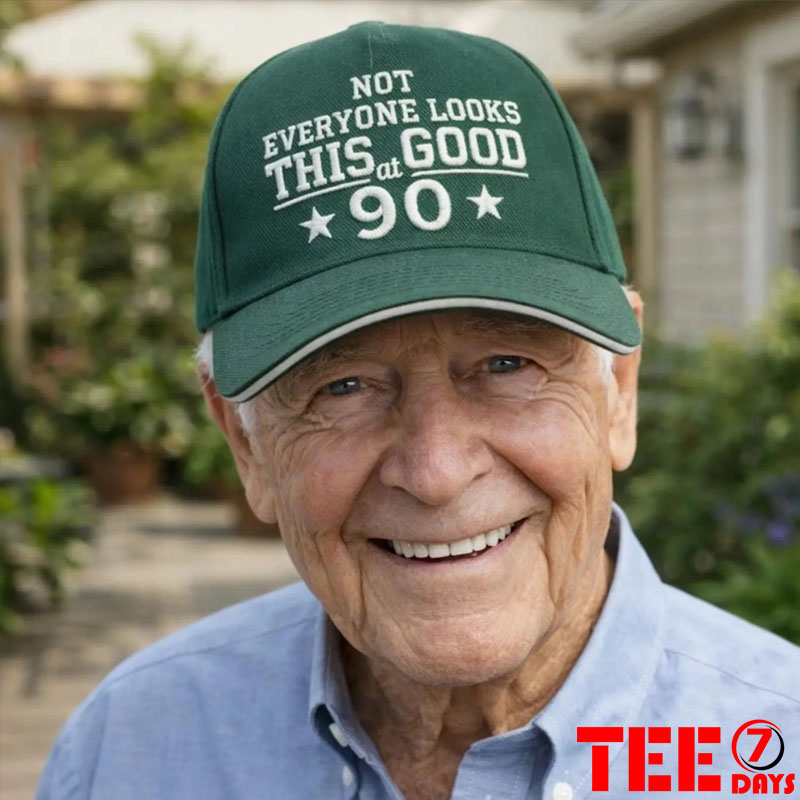 Smiling senior man wearing a forest green baseball cap embroidered with white text reading NOT EVERYONE LOOKS THIS GOOD AT 90 with two stars